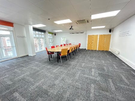 Versatile meeting room in Birmingham with large table and red chairs for workshops.