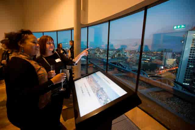 Attendees networking in Shakespeare Memorial Room with city view and digital display.