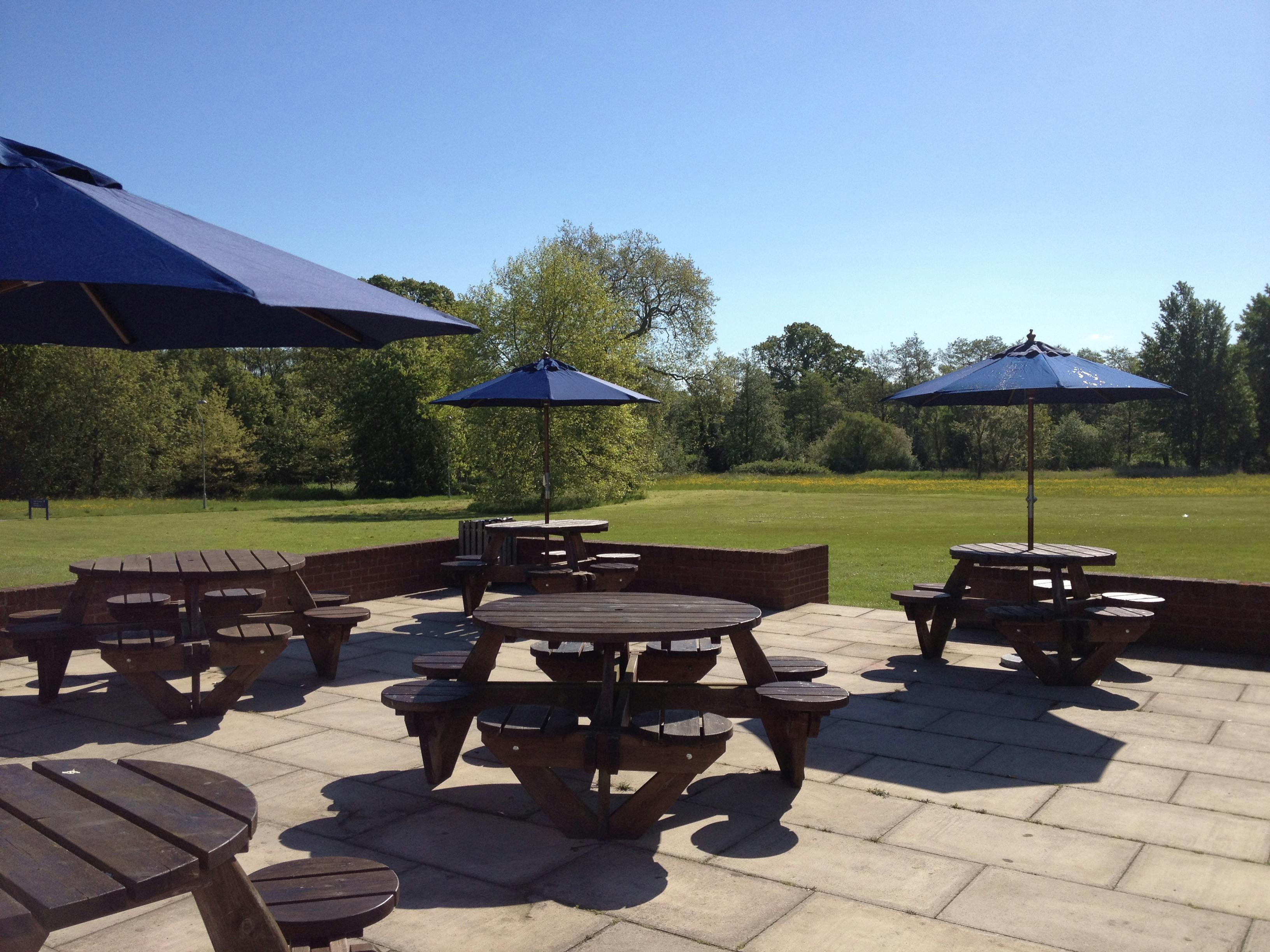 Outdoor seating area with picnic tables and blue umbrellas for casual events at Reading University.