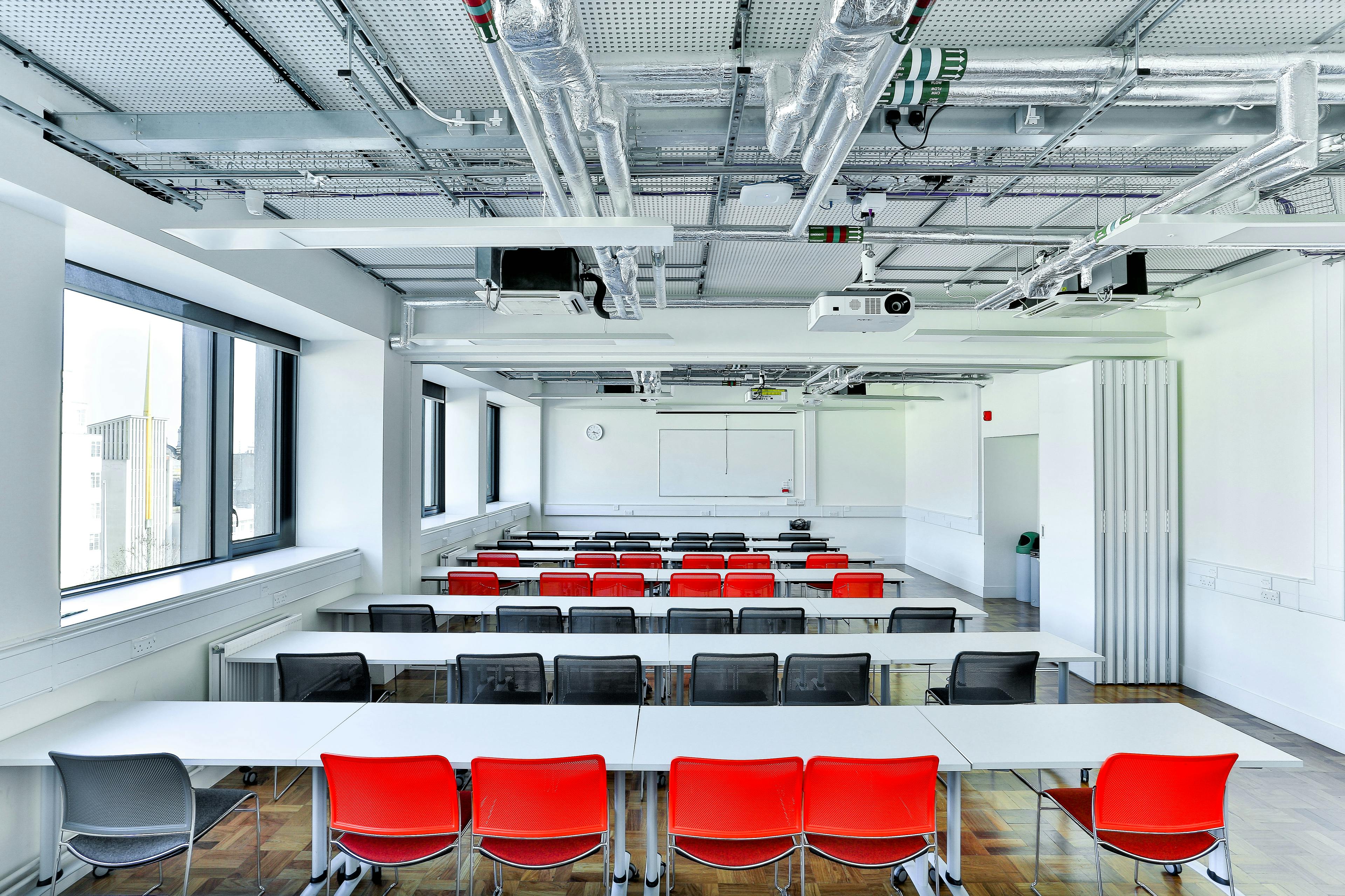 Modern classroom with red and black chairs, ideal for workshops and corporate meetings.