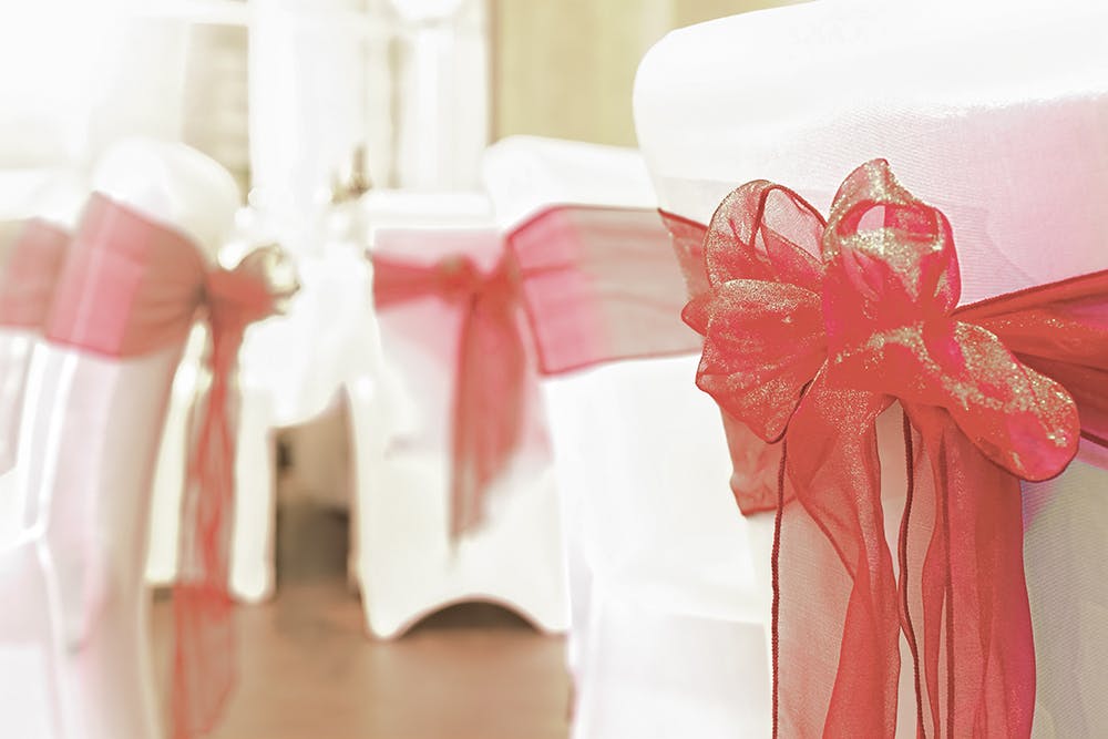 Elegant chair covers with red sashes at The Happenstance for weddings and events.