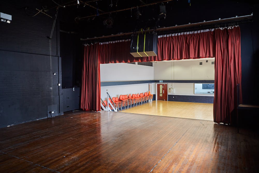 Main Hall at Mill Co. Rose Lipman with stage and red curtains for events and presentations.