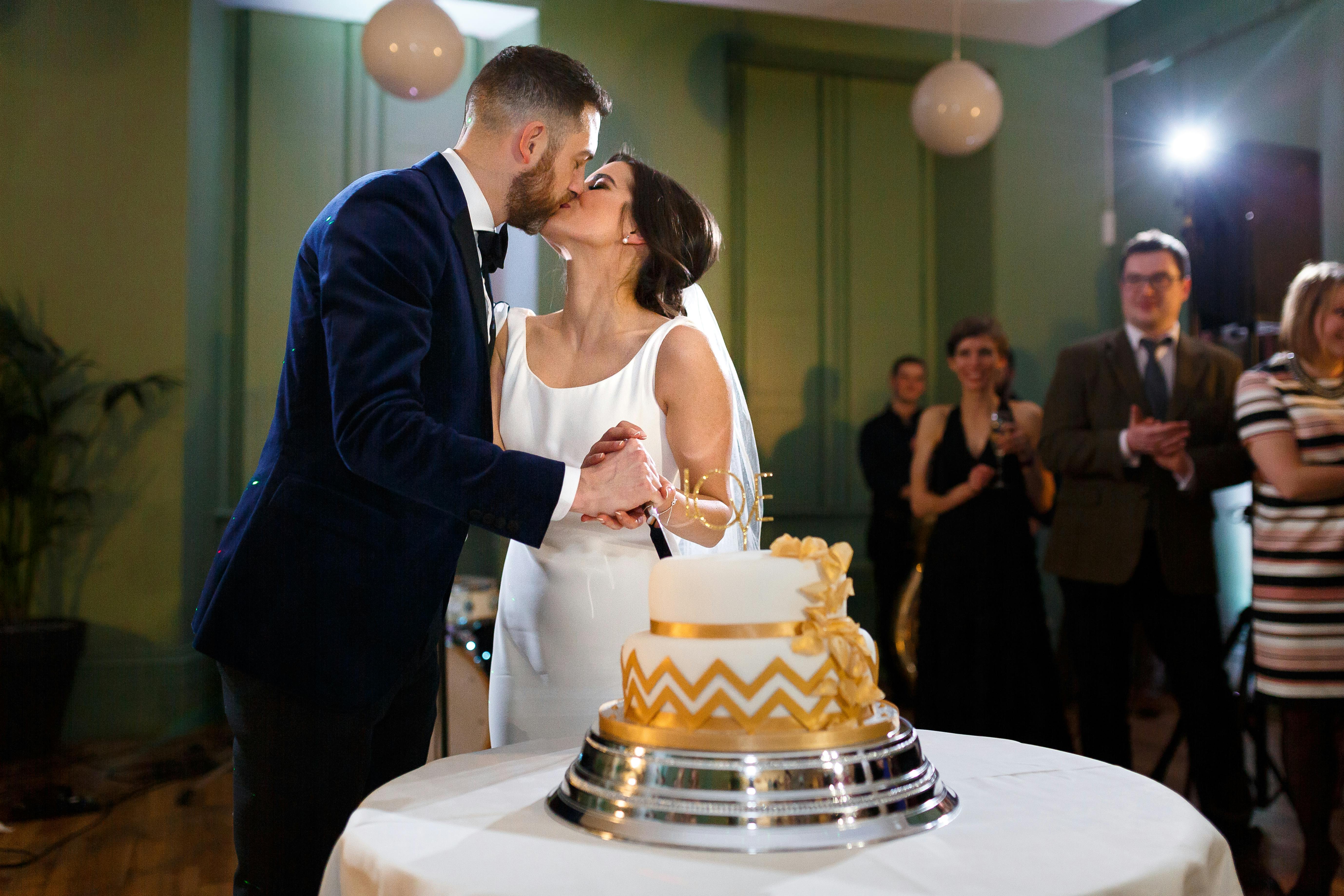 Wedding couple's first kiss beside elegant cake at Manchester Art Gallery.