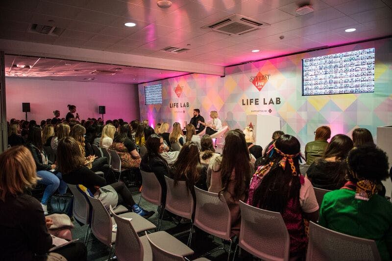 "Engaging conference session in Room B-H, Business Design Centre with vibrant backdrop."